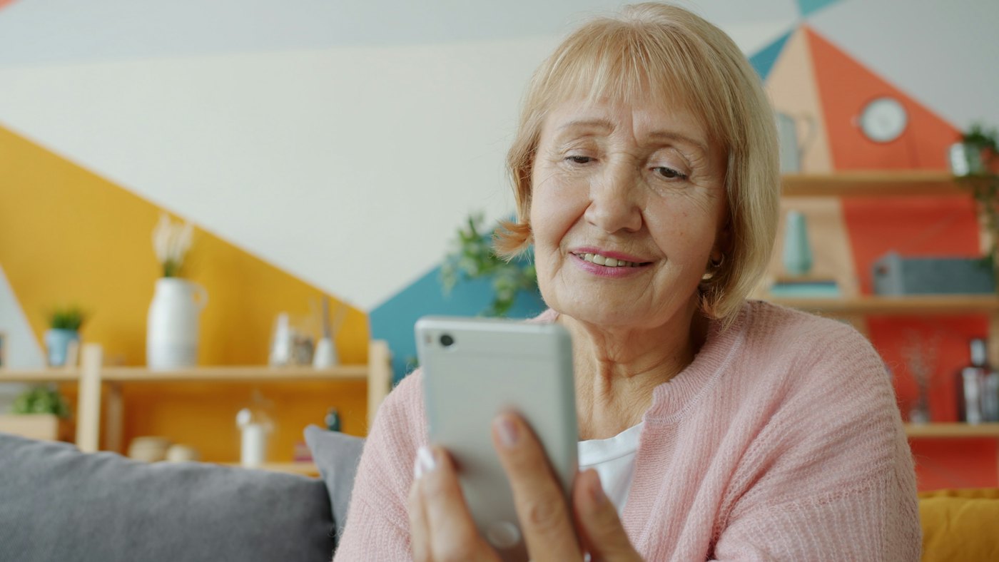 Una mujer mayor sonríe mirando su celular
