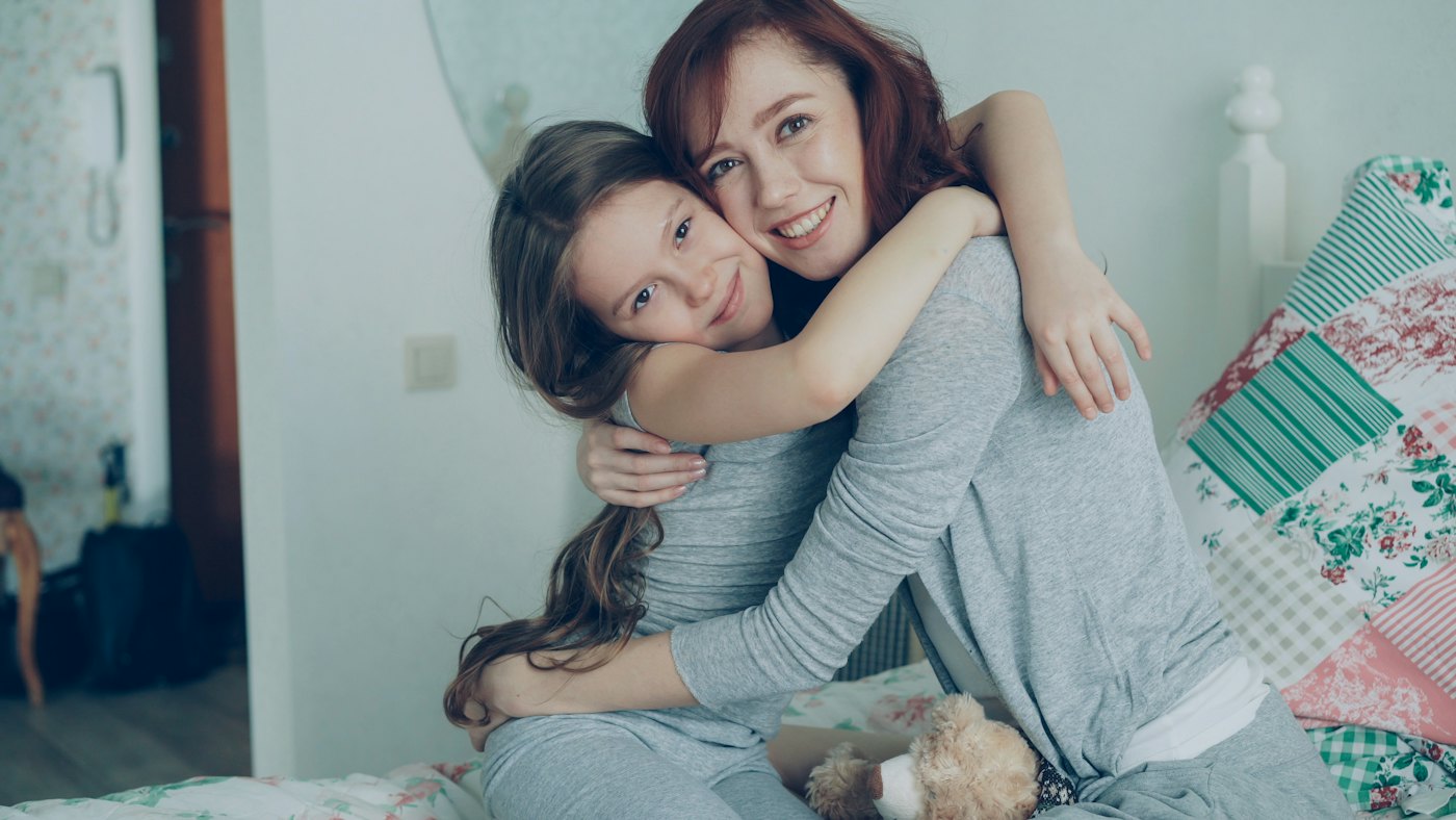 Una madre y su hija se abrazan sonriendo en casa